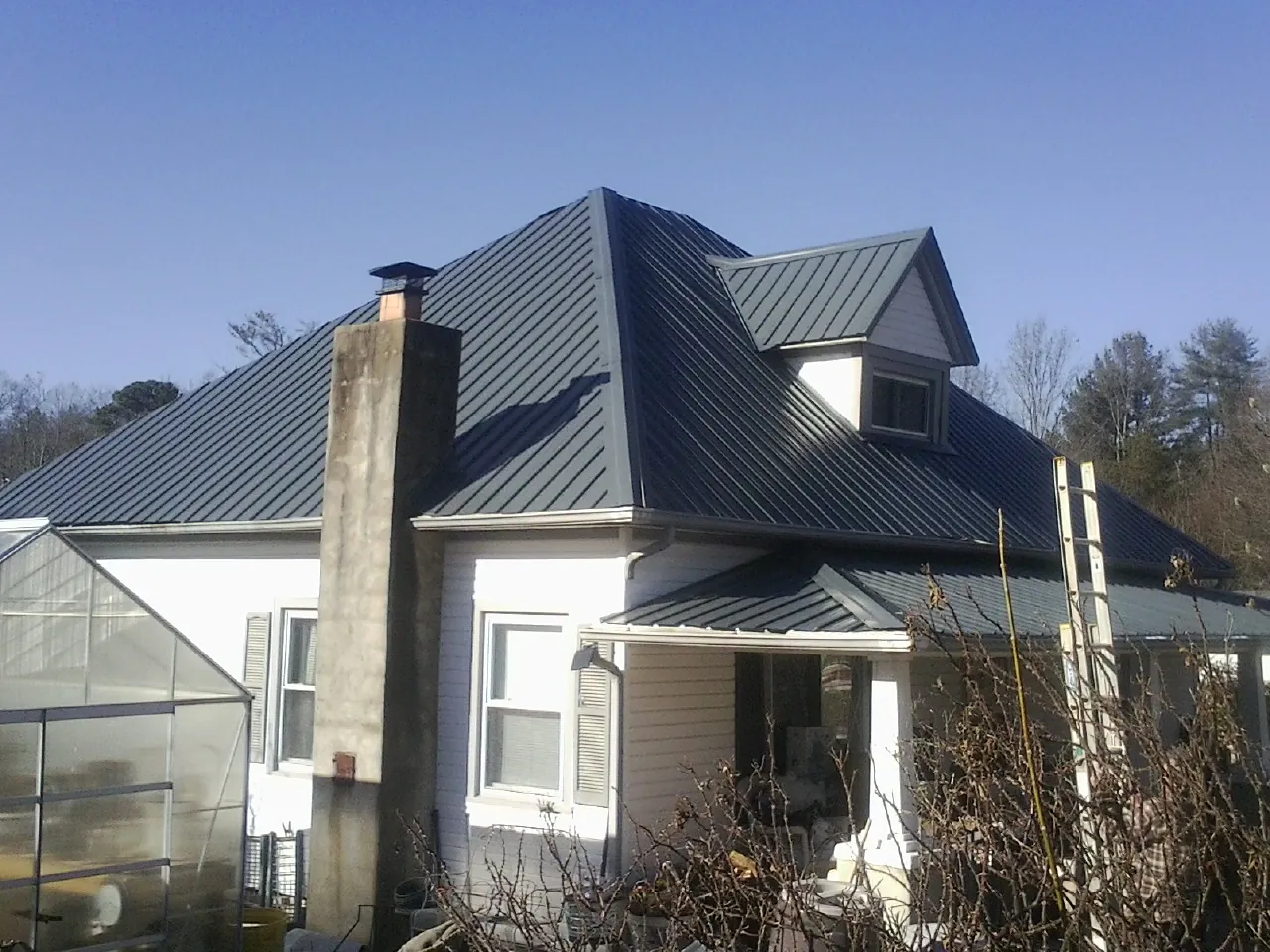 Dark blue standing seam metal roof on a white farmhouse with dormer — Slate & Tile Roof Repair by Roofing Brothers in East Montpelier
