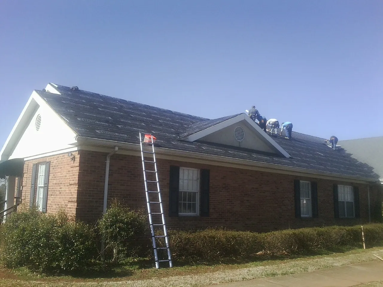 Crew tearing shingles off a brick ranch roof with a ladder set — Emergency Roof Repair work by our crew in East Montpelier