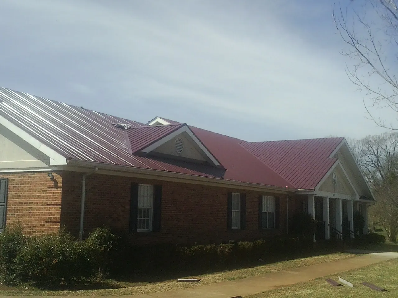 Red metal roof with gabled entries on a long brick building, from a Hail Damage Roof Repair job in East Montpelier