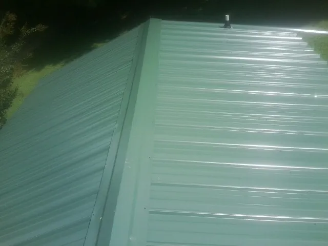 New green metal panels meeting at the ridge of a roof — Flat Roof Repair work by our crew in East Montpelier