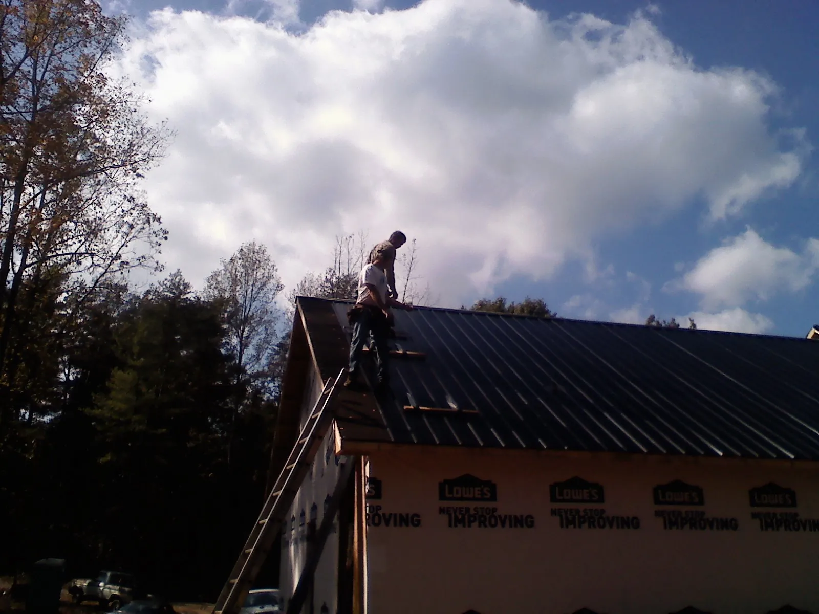 Roofer fastening dark metal panels high against a cloudy sky, from a Roof Inspection job in East Montpelier