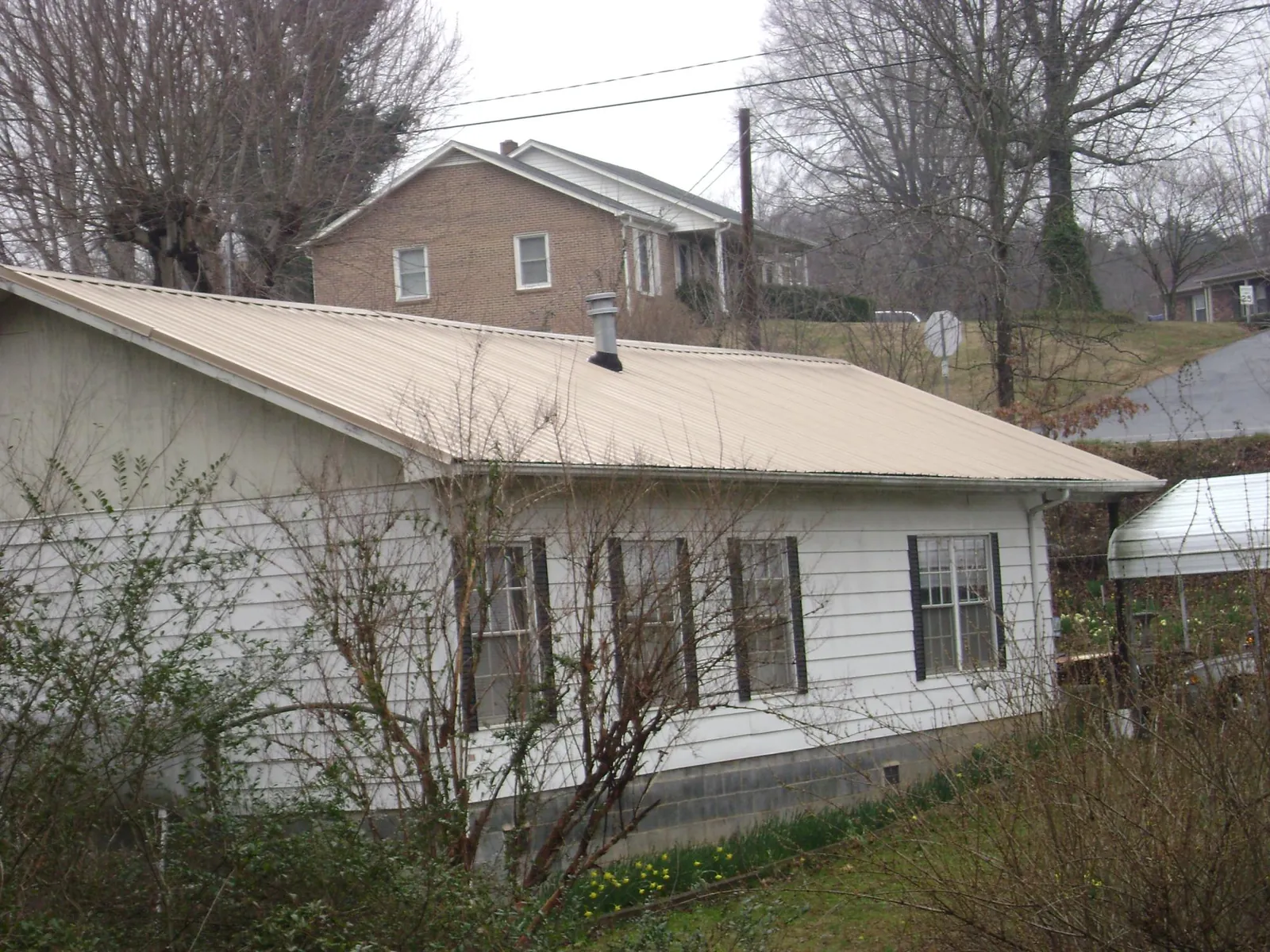 Tan metal roof on a white sided house set into a hillside — Commercial Roofing by Roofing Brothers in East Montpelier