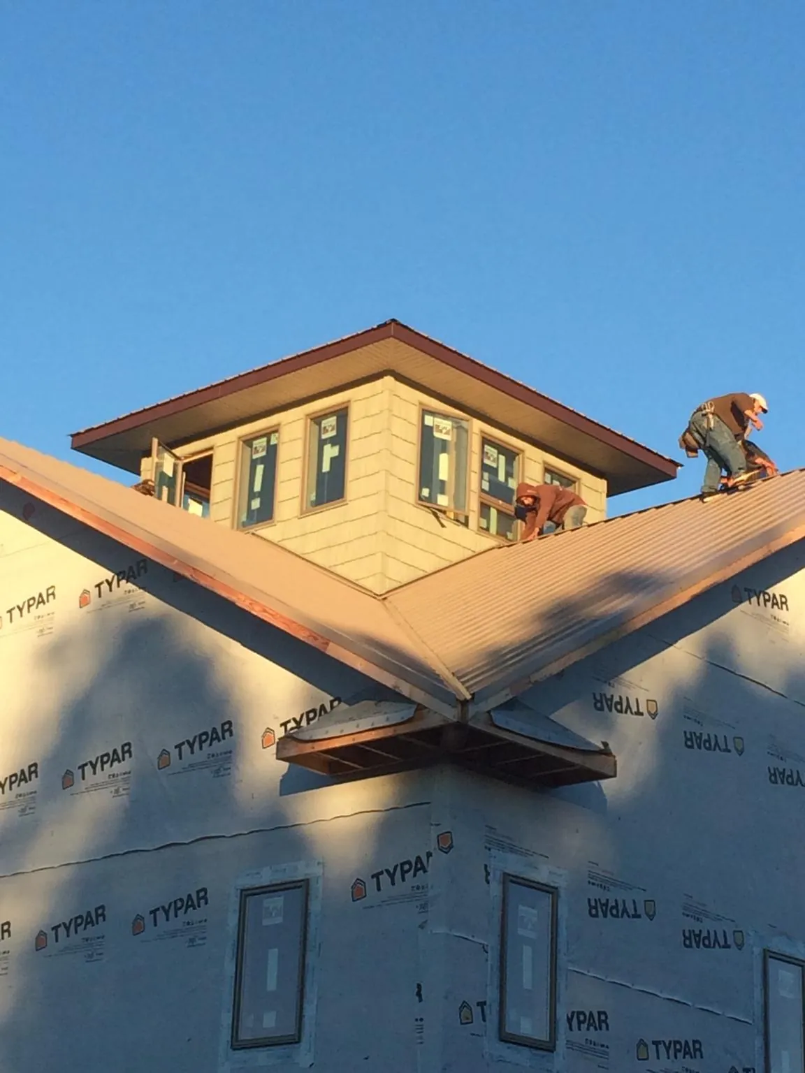 Roofers working around a rooftop cupola on a new metal roof at sunset — Roof Waterproofing in East Montpelier by Roofing Brothers